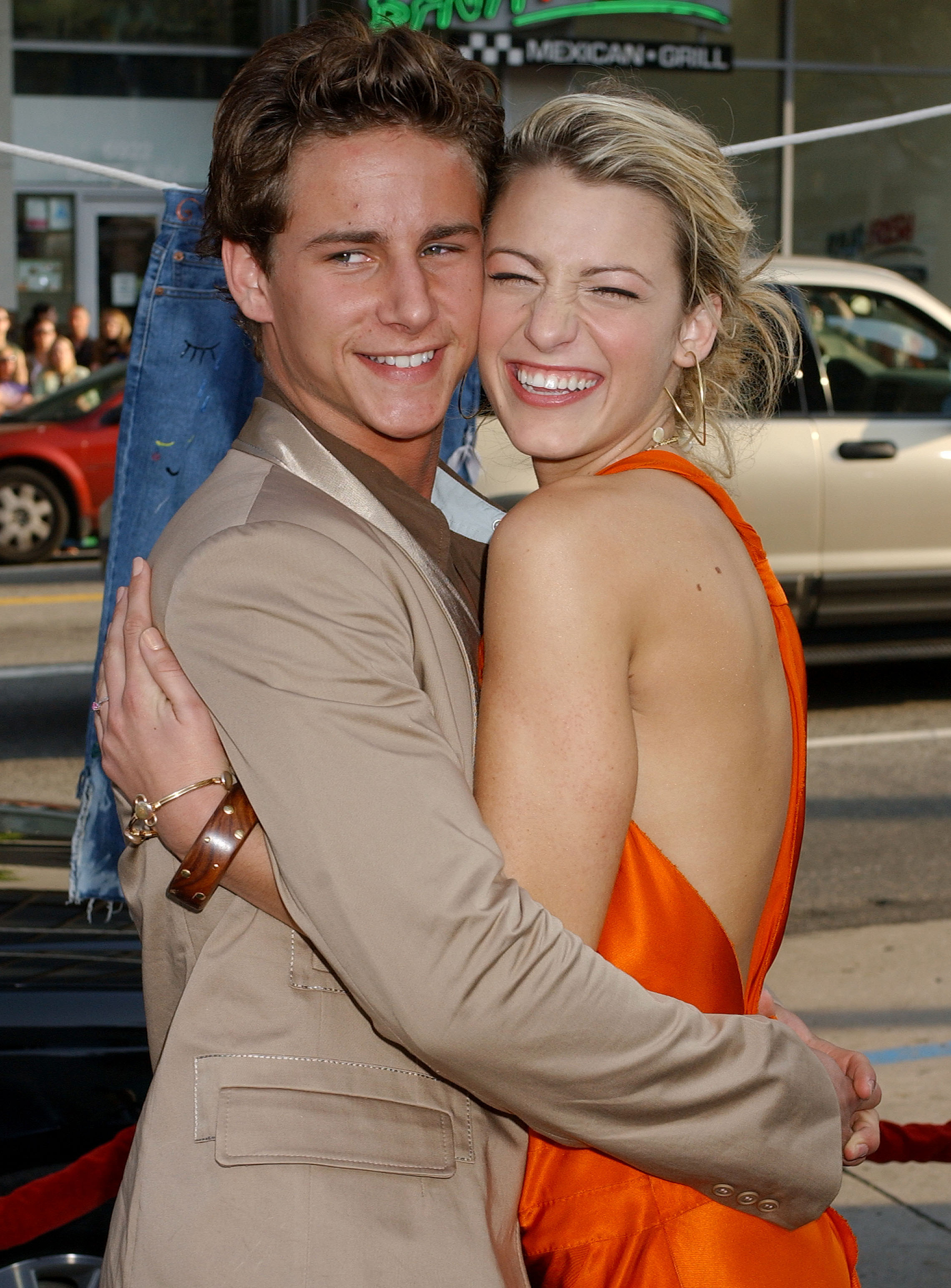 Blake and Kelly embracing, she in an orange dress and he in a beige suit