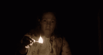 Persona encendiendo una cerilla en un entorno oscuro, expresión seria y concentrada