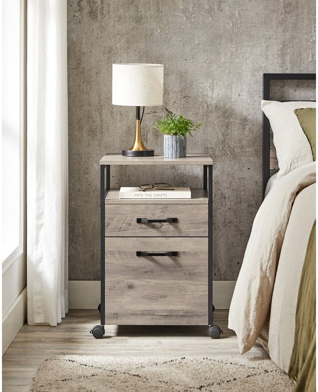 Bedside table with lamp and plant beside a bed, featuring minimalist design ideal for home decor