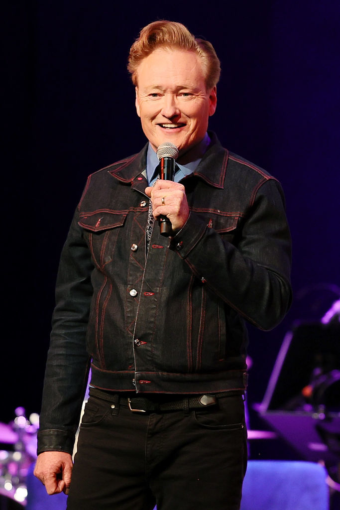 Comedian in denim jacket and black pants performing on stage with microphone