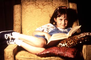 mara wilson as matilda sitting in a chair reading a book