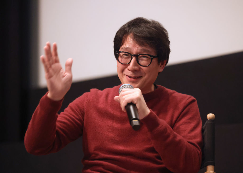 Ke Huy Quan in a red sweater speaking into a microphone during a discussion