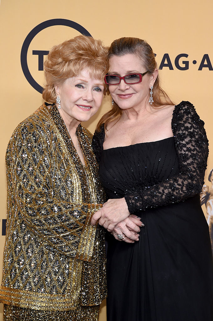 Debbie Reynolds in a shimmery outfit with a prominent pattern and Carrie Fisher in a black lace dress, standing closely together