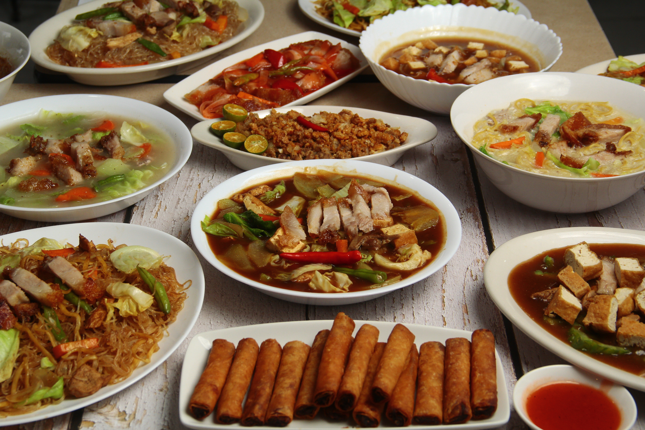 Assortment of Asian dishes, including noodles, spring rolls, and soups on a wooden table