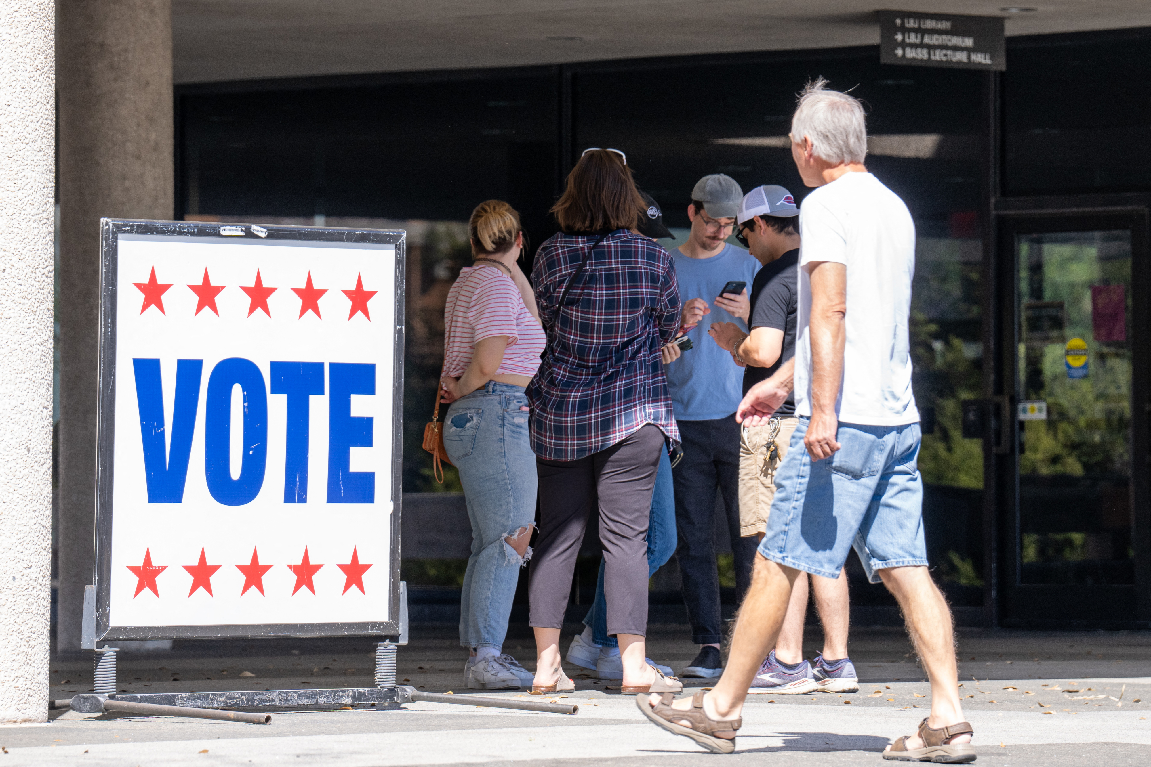 A group of people by a &#x27;VOTE&#x27; sign with stars, indicating a polling station entrance