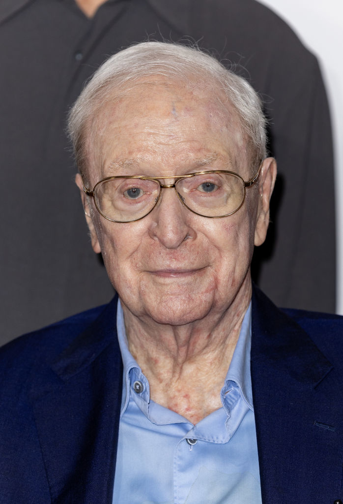 Close-up of Michael Caine in a navy jacket and shirt wearing glasses