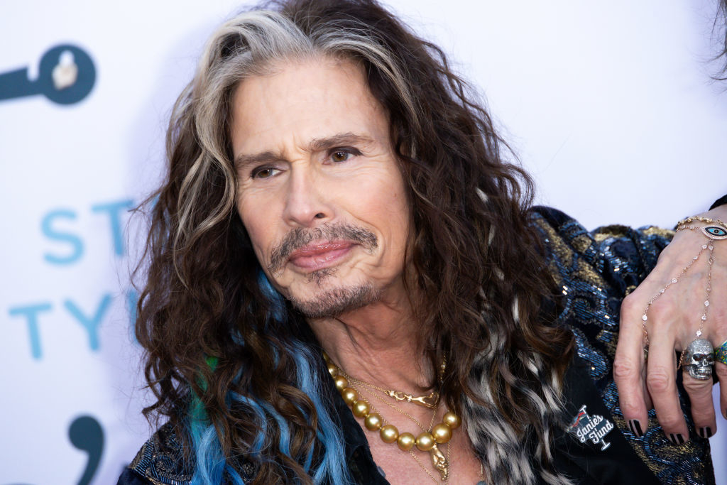 Steven Tyler in a patterned jacket with layered necklaces, attending an event