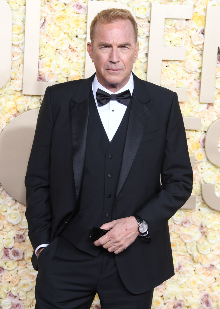 Kevin in a black tuxedo with bow tie, posing at an event, standing in front of a floral backdrop
