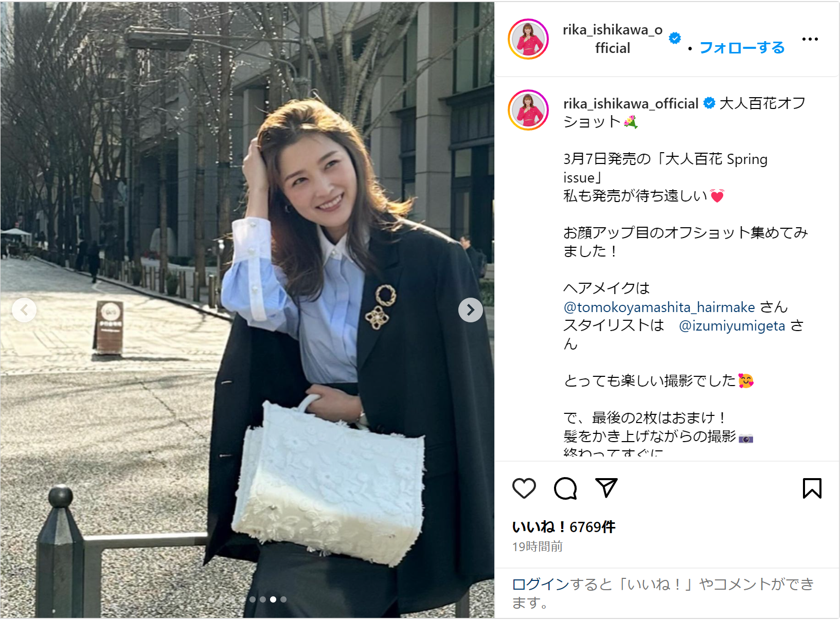 石川梨華がスーツにブローチ、白いバッグを持ち、都会の通りでポーズをとっています。