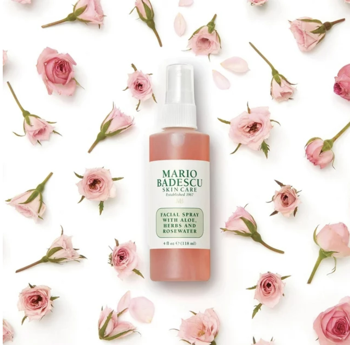 Mario Badescu facial spray bottle with roses scattered around on a plain background