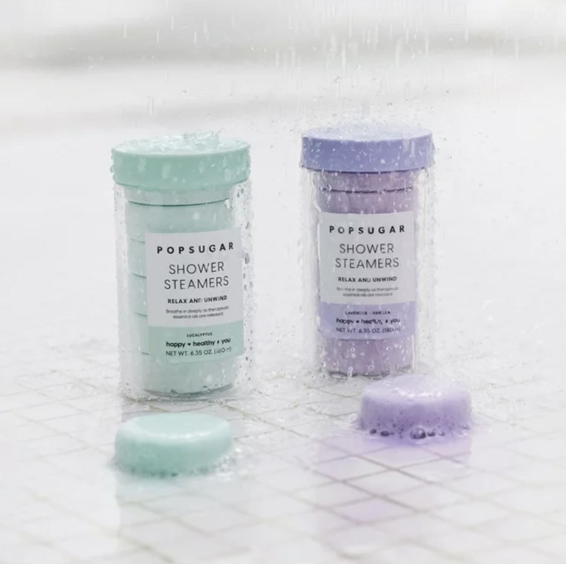 Two shower steamer bottles with tablets on a wet surface, labeled &quot;POPSUGAR&quot; for relaxation