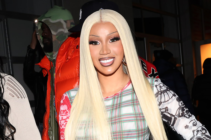 Cardi B smiling in plaid dress, long ombre hair, at a music event