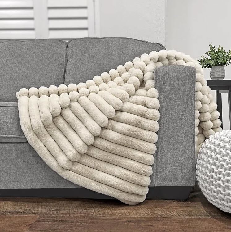 A chunky knitted blanket draped over a gray couch in a living room setting