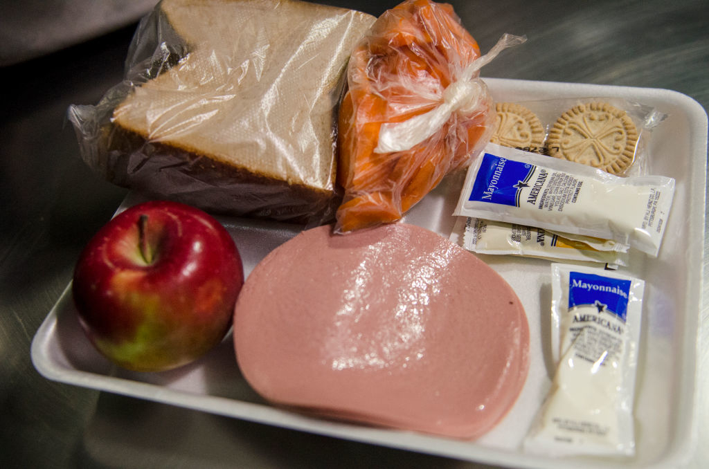 A jail lunch tray with a sandwich, apple, cookies, and packaged condiments