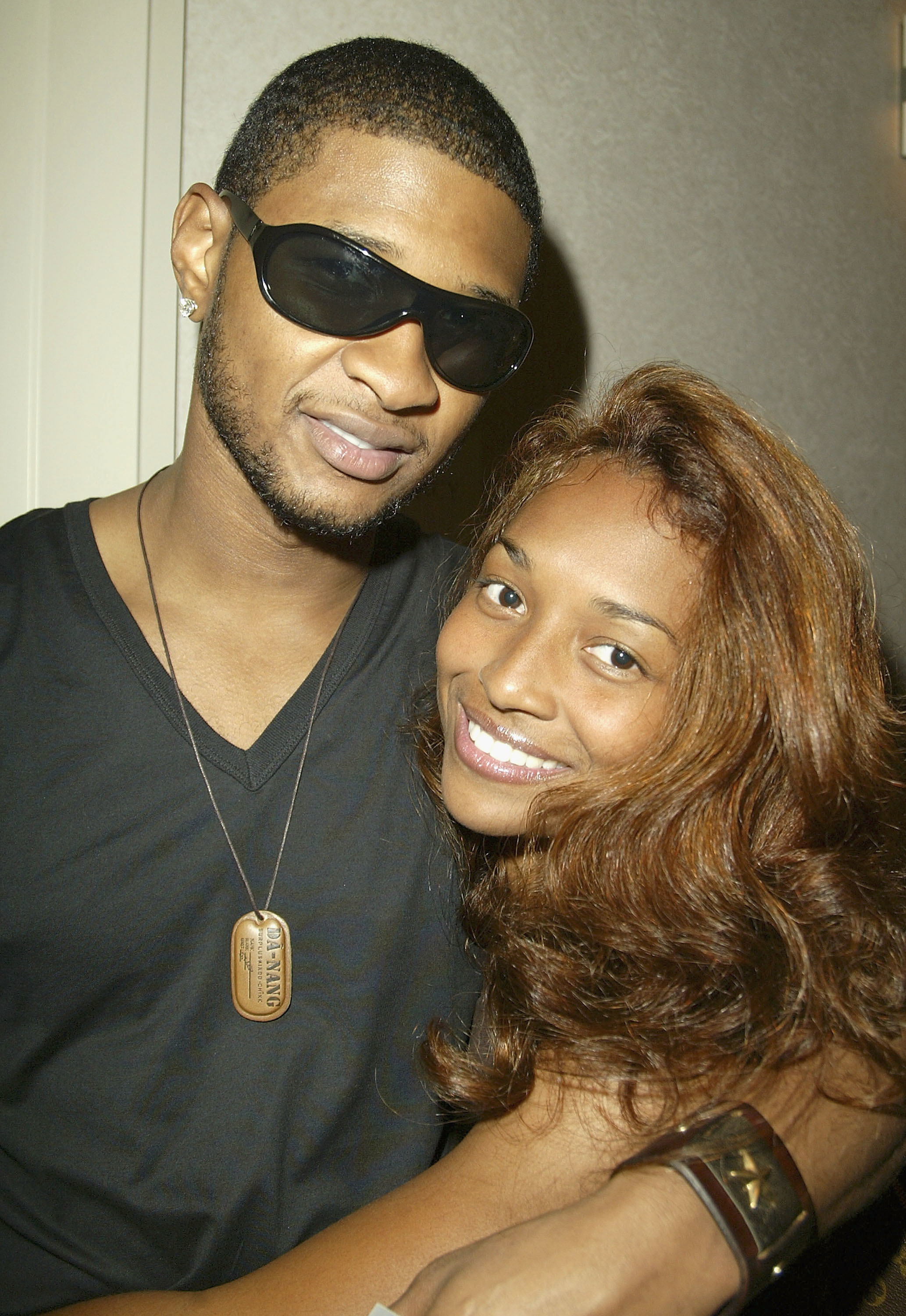 Usher smiling and wearing sunglasses and a V-neck top and Chilli smiling and embracing