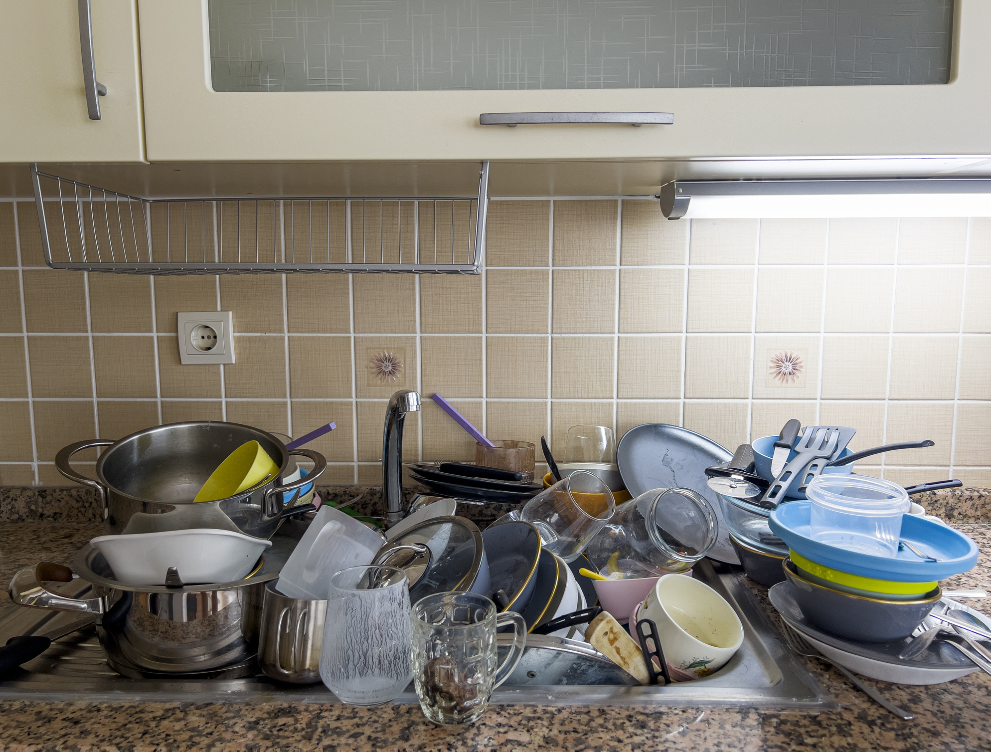 A cluttered kitchen sink piled with various unwashed dishes and utensils
