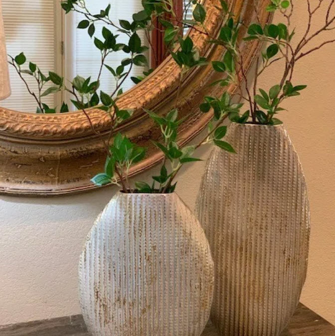 Two textured vases with plants beside a round mirror