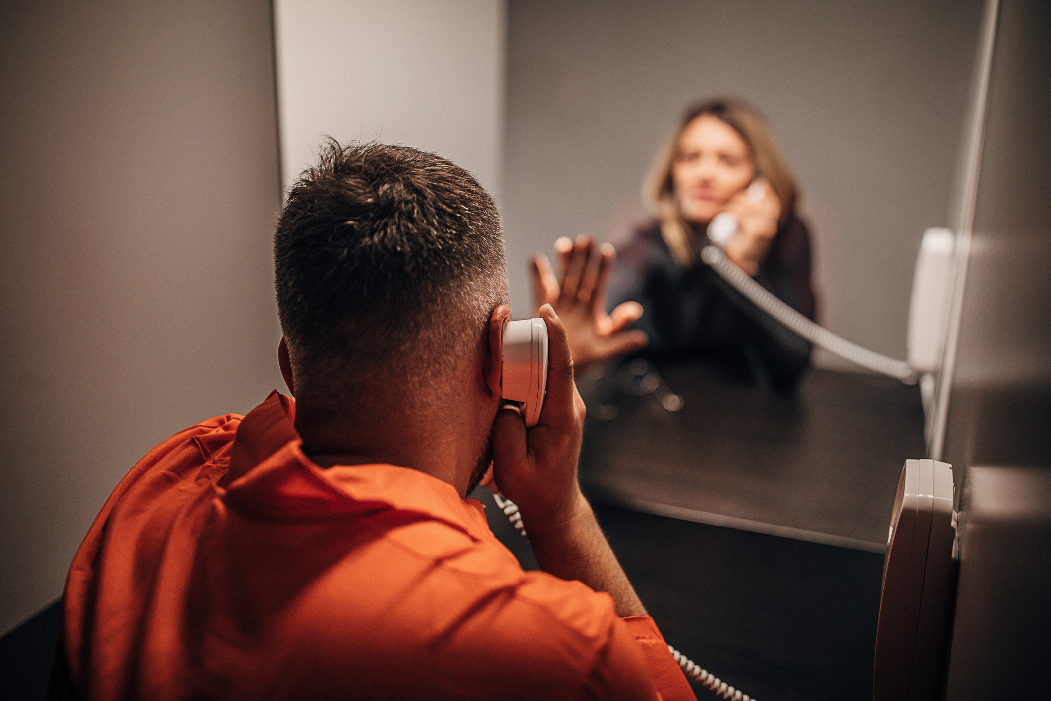 Prisoner speaks over phone behind a reflective glass with another individual on the other