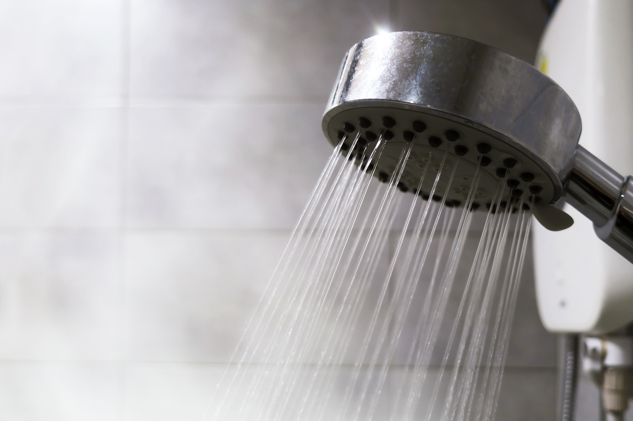 Water flows from a showerhead against a tiled wall background
