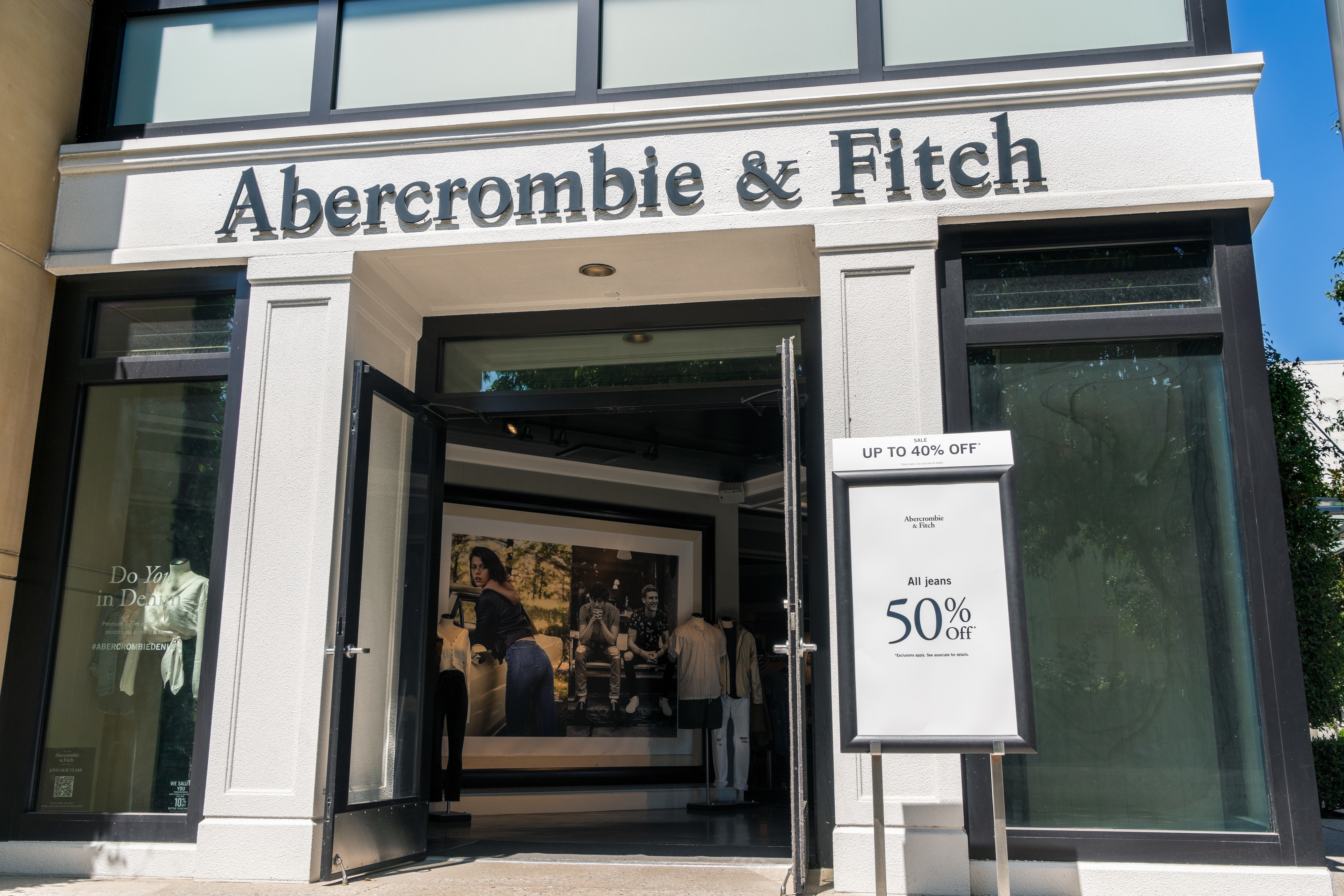 Storefront of Abercrombie &amp;amp; Fitch with promotional signs for discounts in the window