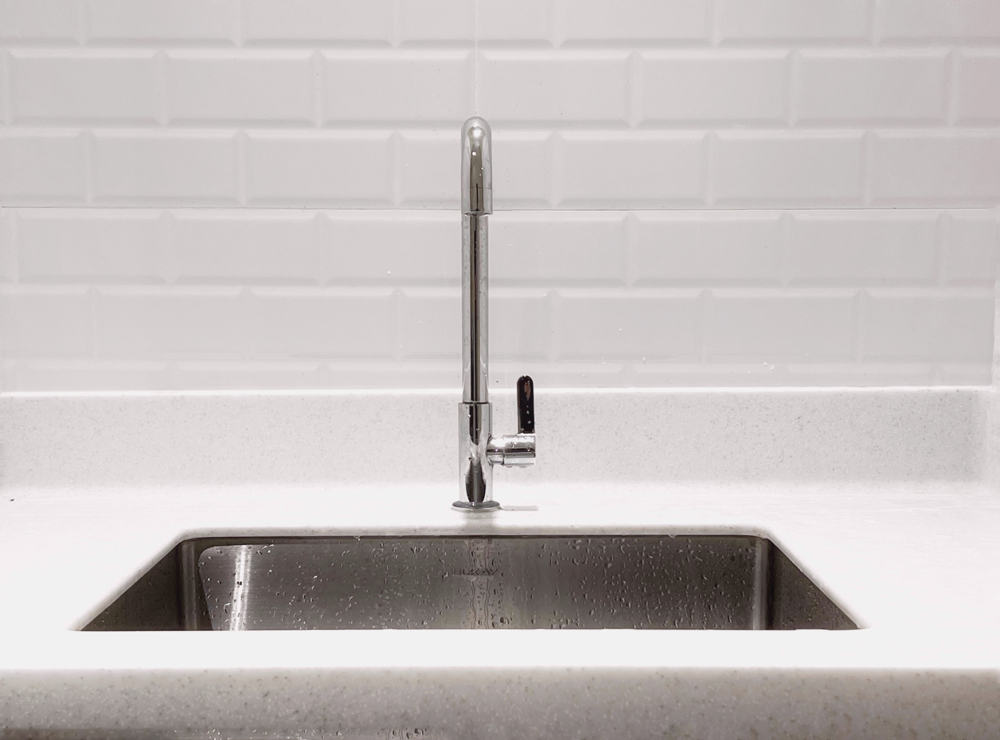 Stainless steel kitchen sink and faucet against a white tile backsplash