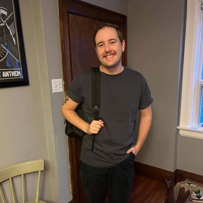 Un homme souriant, debout à l'intérieur avec un sac à dos sur une épaule