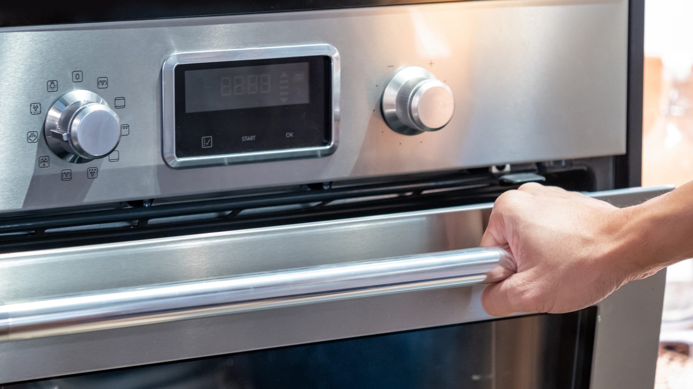 Person opening a modern oven door with digital display and control knobs