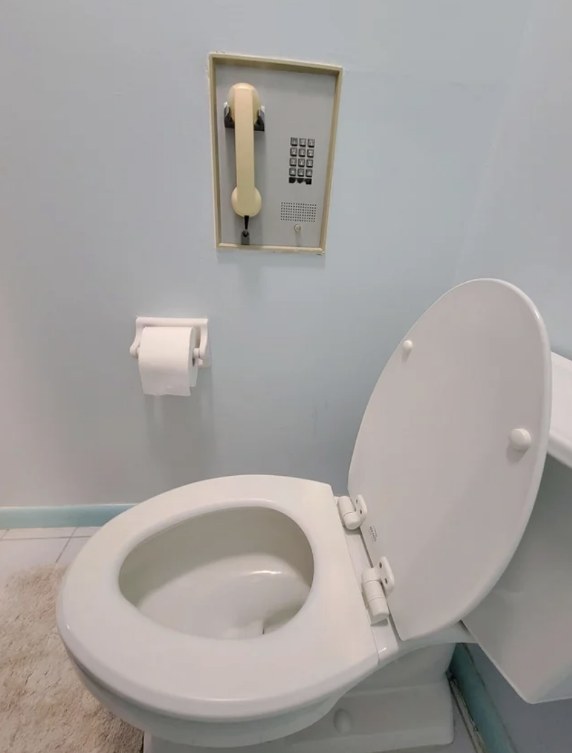 A bathroom with an old-fashioned phone mounted on the wall above the toilet