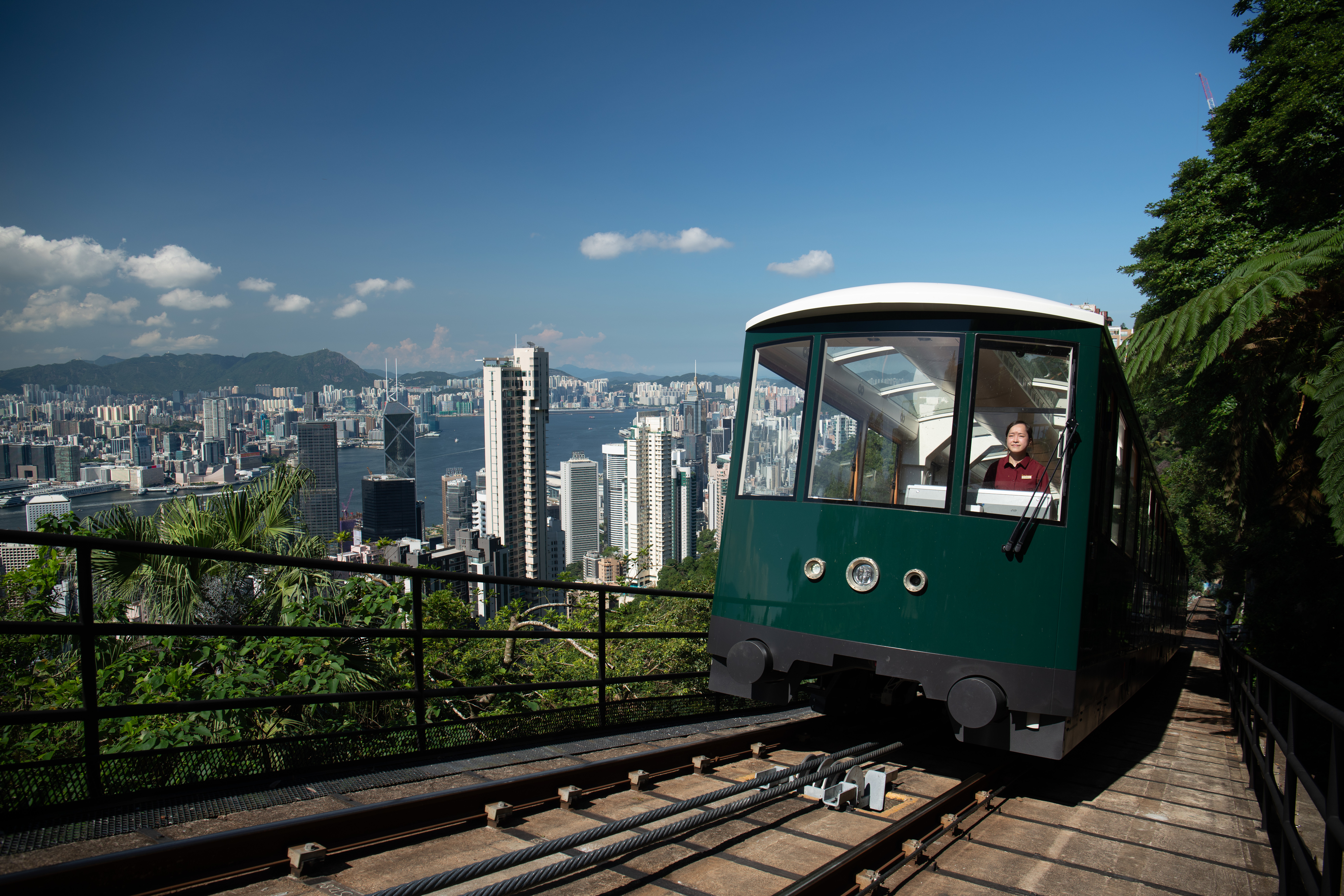 A tram on a steep track with a scenic view of a city skyline, with a person visible through the window