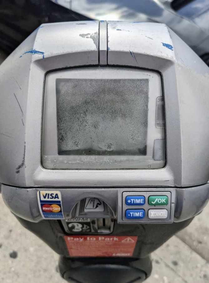 An old parking meter with a faded screen and payment stickers, showing signs of wear and tear