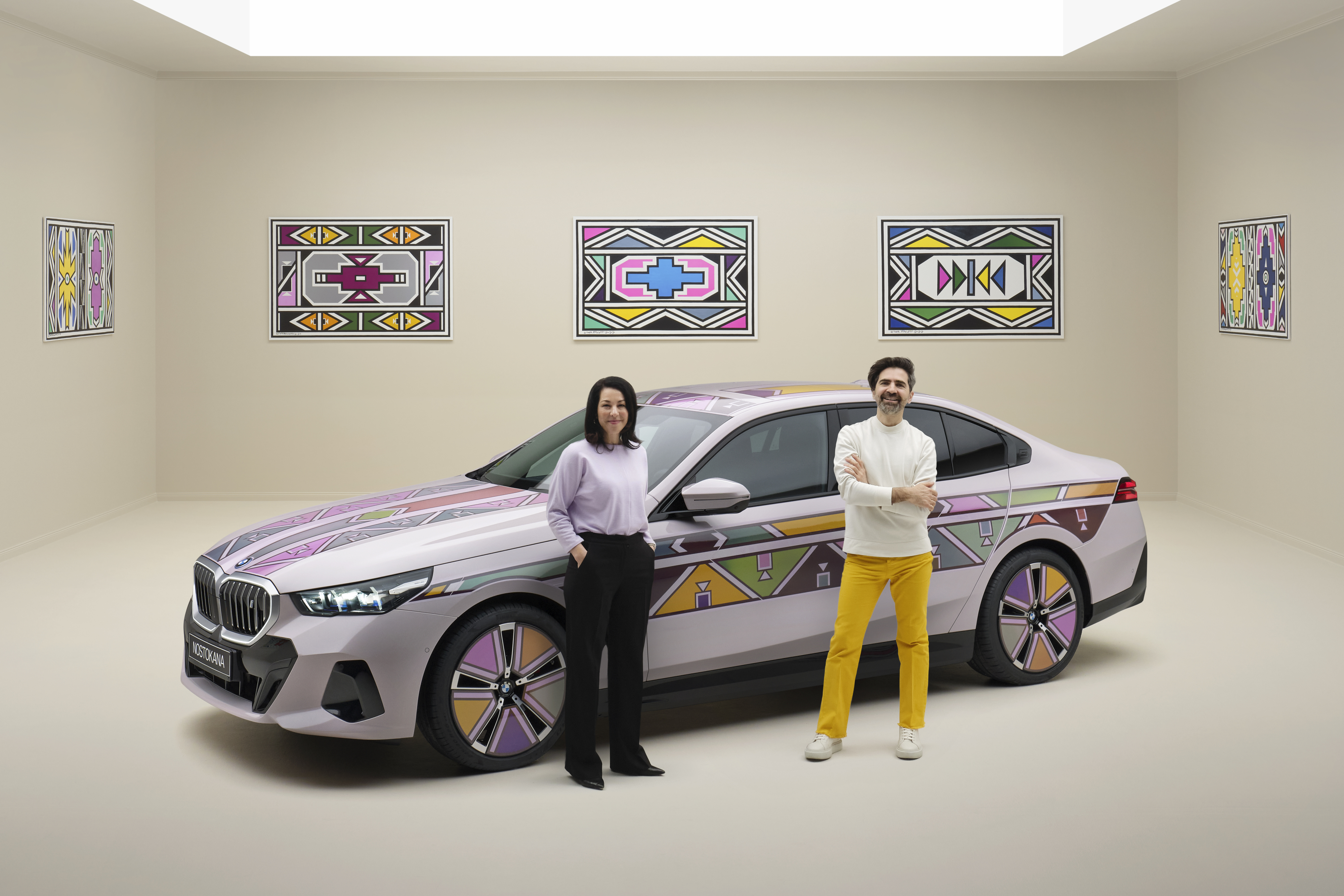 Two people standing beside a custom-painted car with geometric art on the walls, reflecting a contemporary style