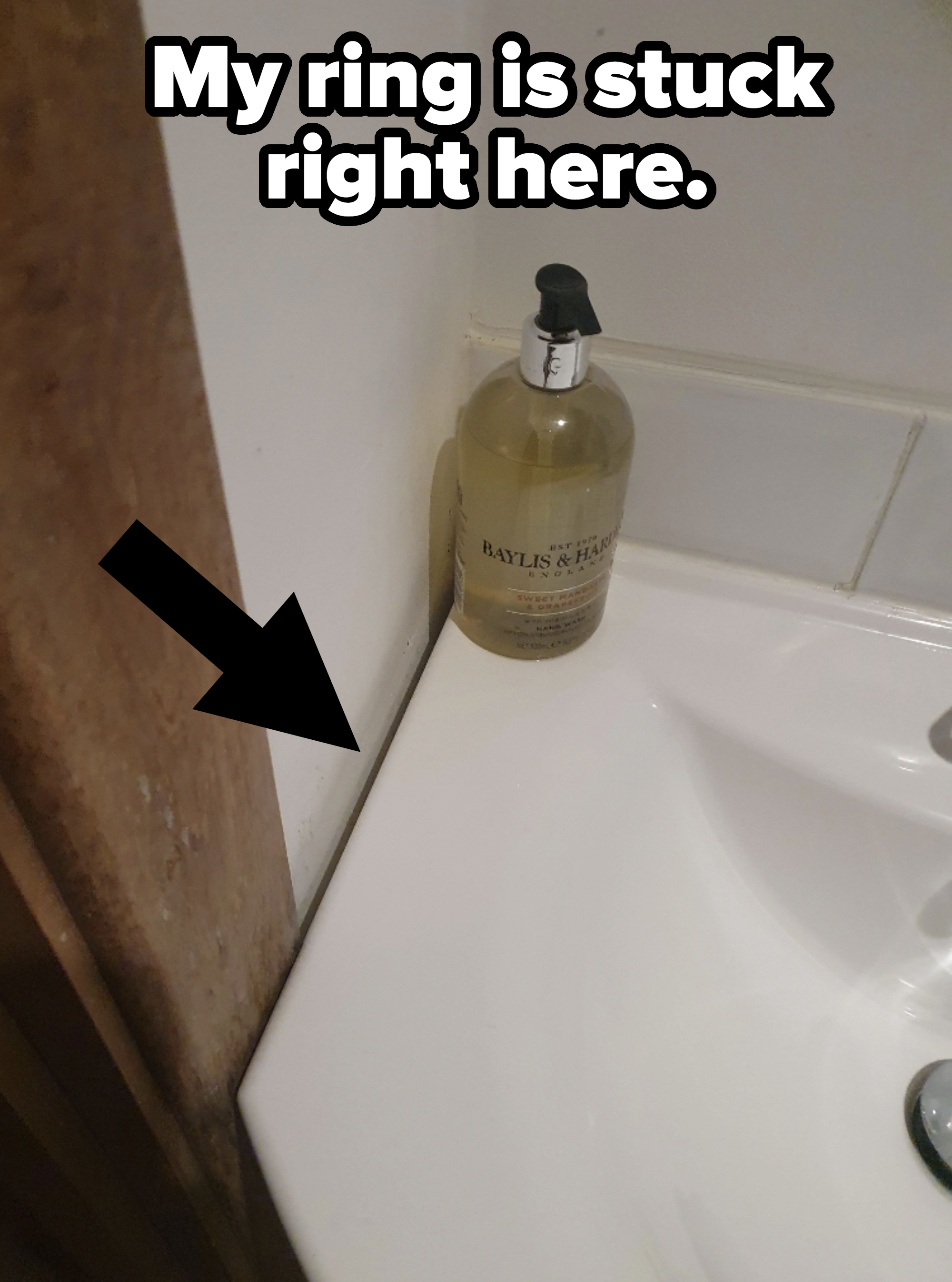 Bottle of hand soap on a bathroom sink counter next to a wall, with arrow pointing to gap between wall and sink, with caption, &quot;My ring is stuck right here&quot;