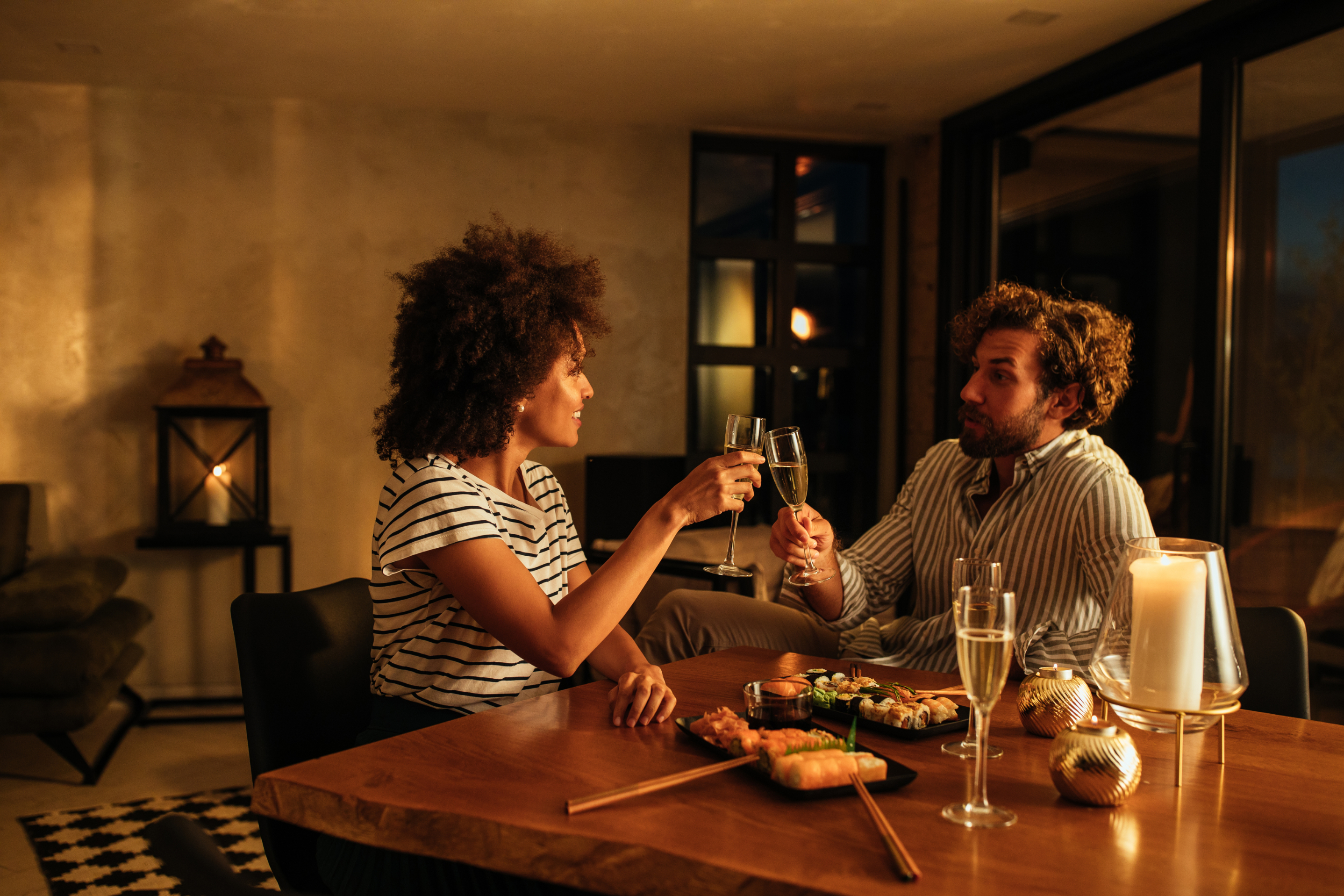 Two people having a candlelit dinner and toasting with wine glasses