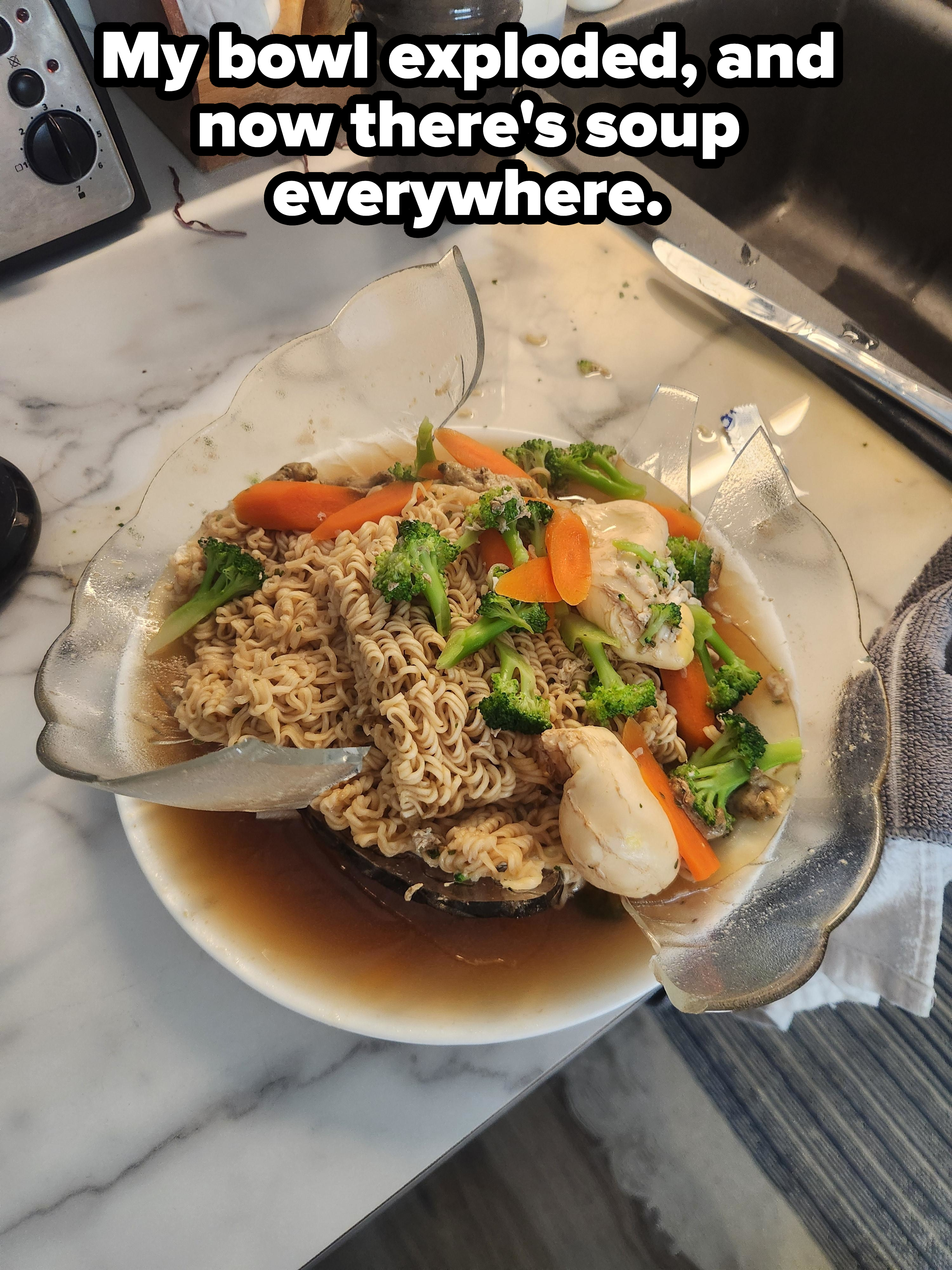 A bowl of noodle soup with vegetables and shrimp on a kitchen counter, with part of the bowl shattered, with caption, &quot;My bowl exploded, and now there&#x27;s soup everywhere&quot;