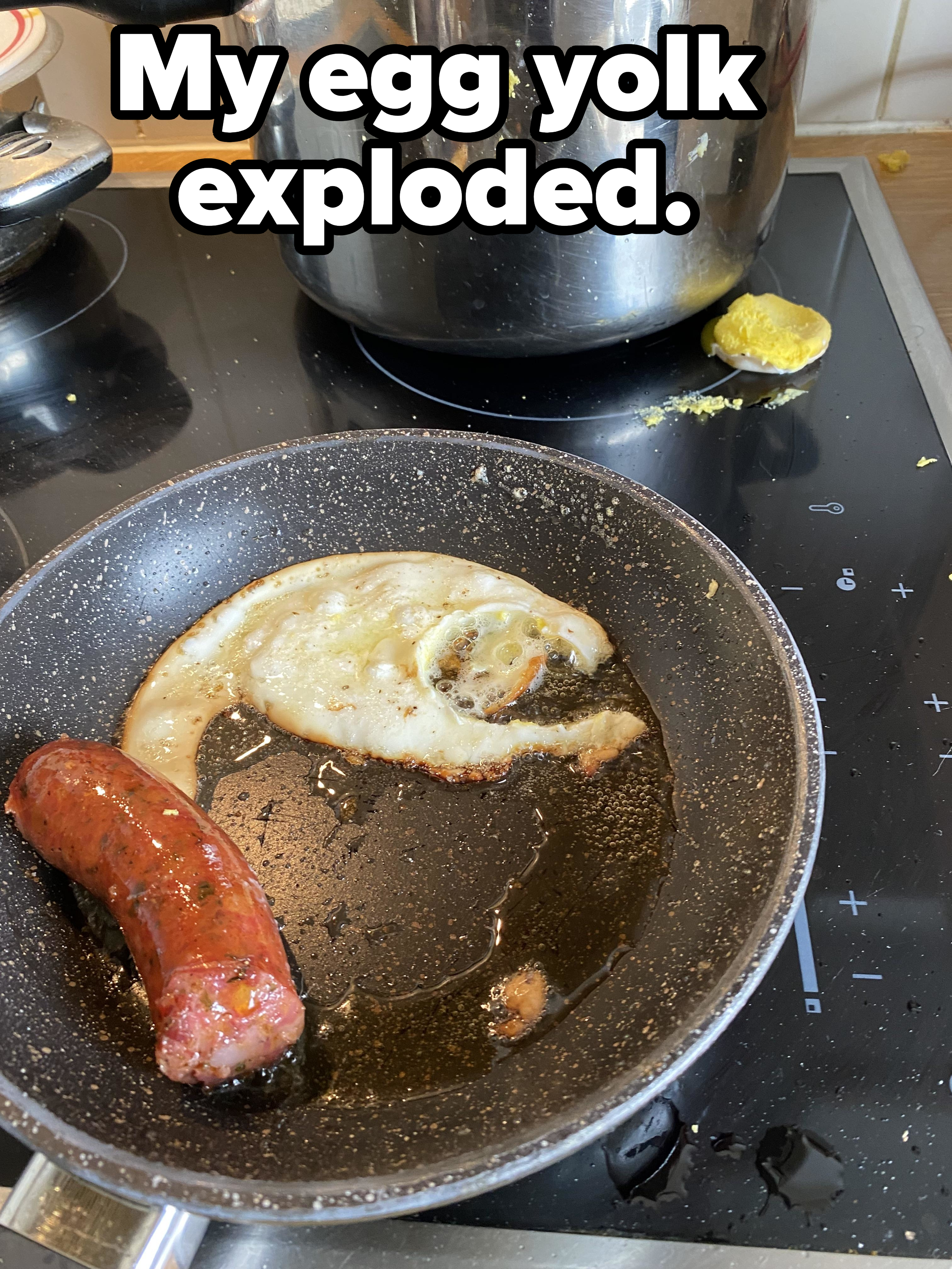 Frying pan on a stove containing one sausage and a partially cooked, misshapen fried egg missing the yolk, which is now on the stovetop, with caption &quot;My egg yolk exploded&quot;