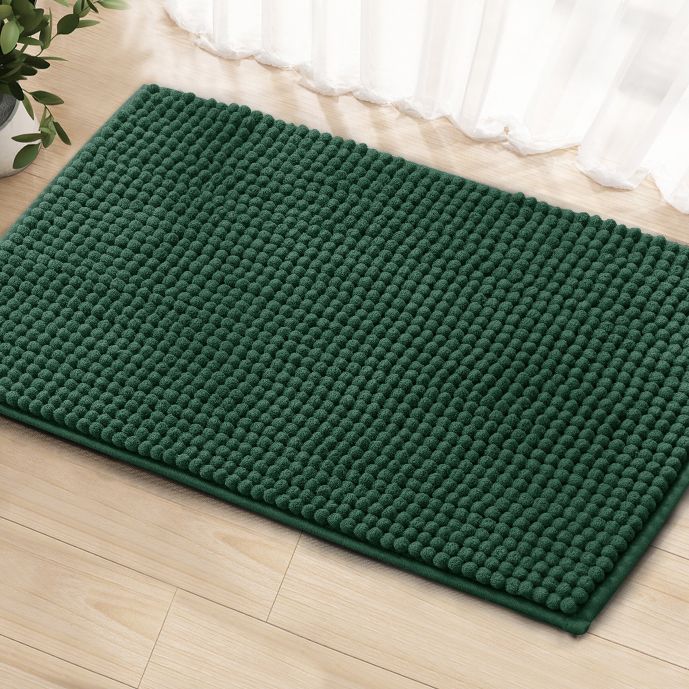 Green textured doormat on a wooden floor near a sheer curtain