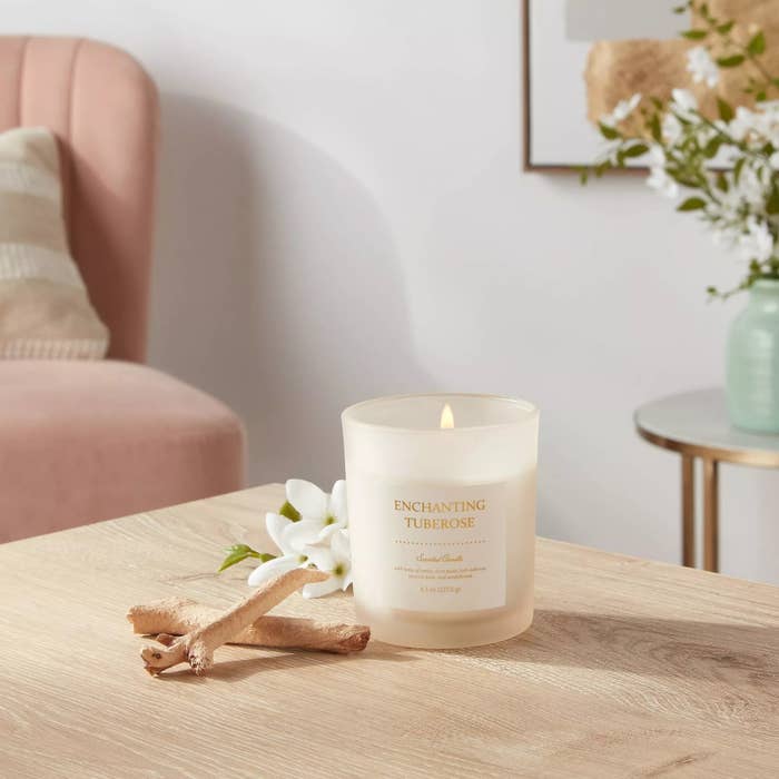 Lit tuberose-scented candle on a table with flowers in the background