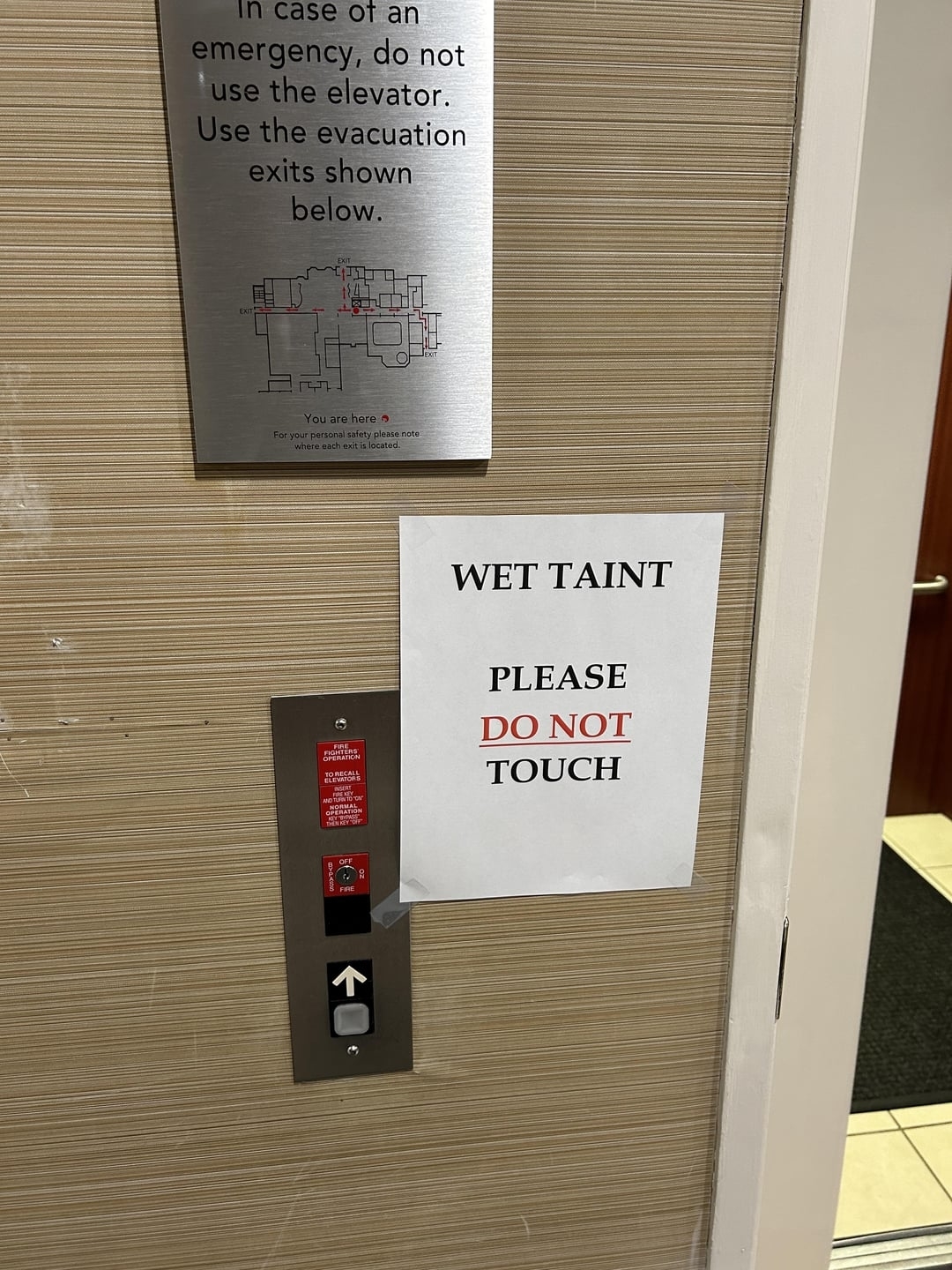 Sign next to an elevator reads &quot;PLEASE T&#x27; AINT DO NOT TOUCH&quot; with a diagram of evacuation routes above it