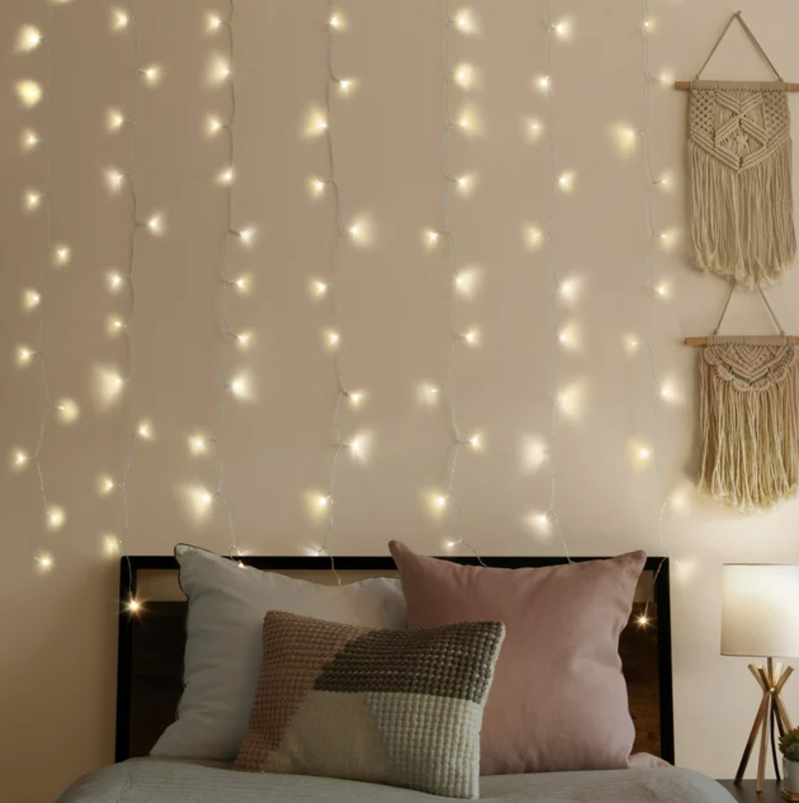 String lights hung on a wall above a bed with decorative pillows