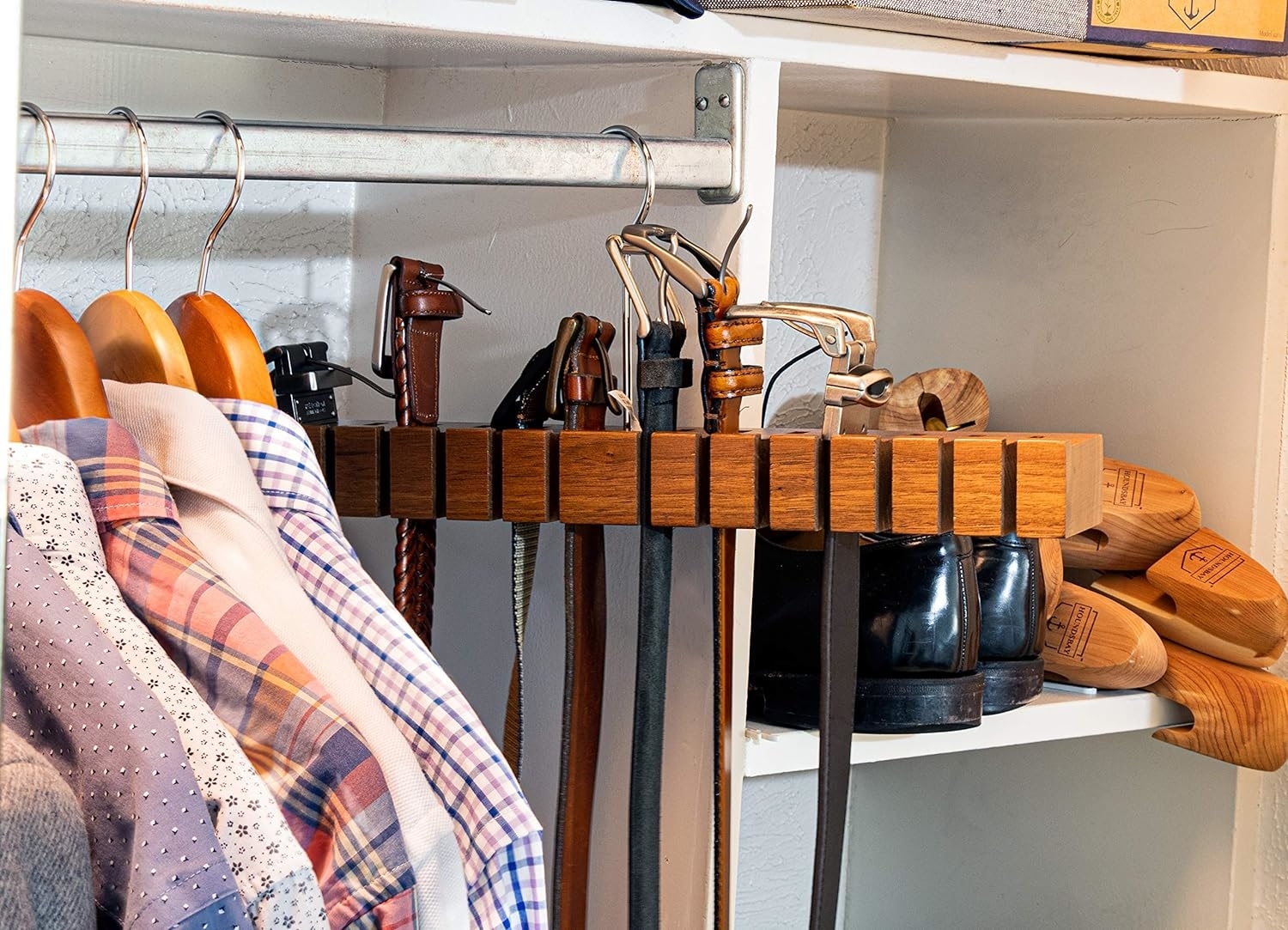 Closet organizer with shirts on hangers, wooden shoe racks with shoes, and belts hanging above