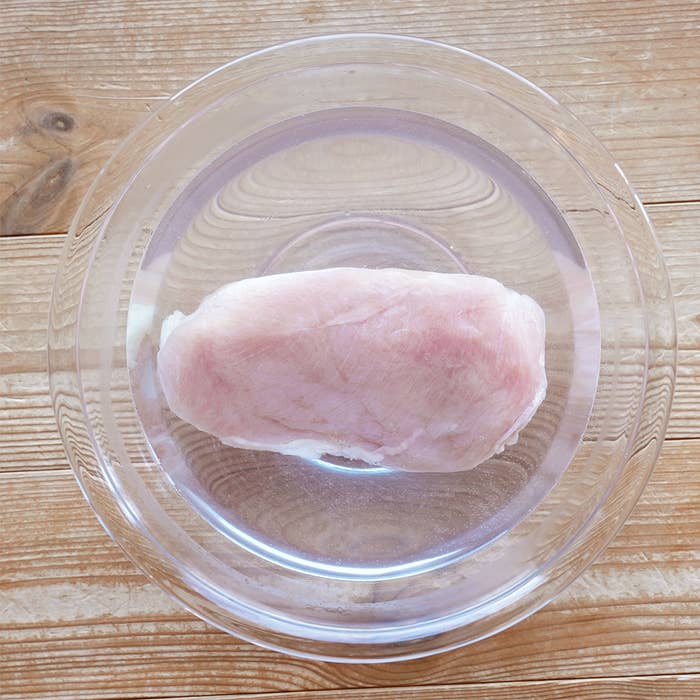 透明なボウルに入った解凍中の生の鶏むね肉。