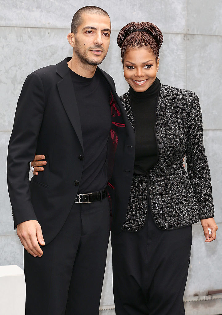 Wissam and Janet standing side by side smiling; individual on left in a black suit, person on right in a tweed-style jacket and pants