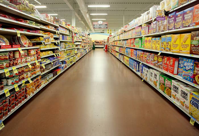 Grocery store aisle with various packaged foods on shelves, person in red shirt at the end