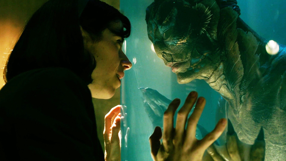 Woman faces a humanoid amphibian creature separated by glass, both touching the surface with hands