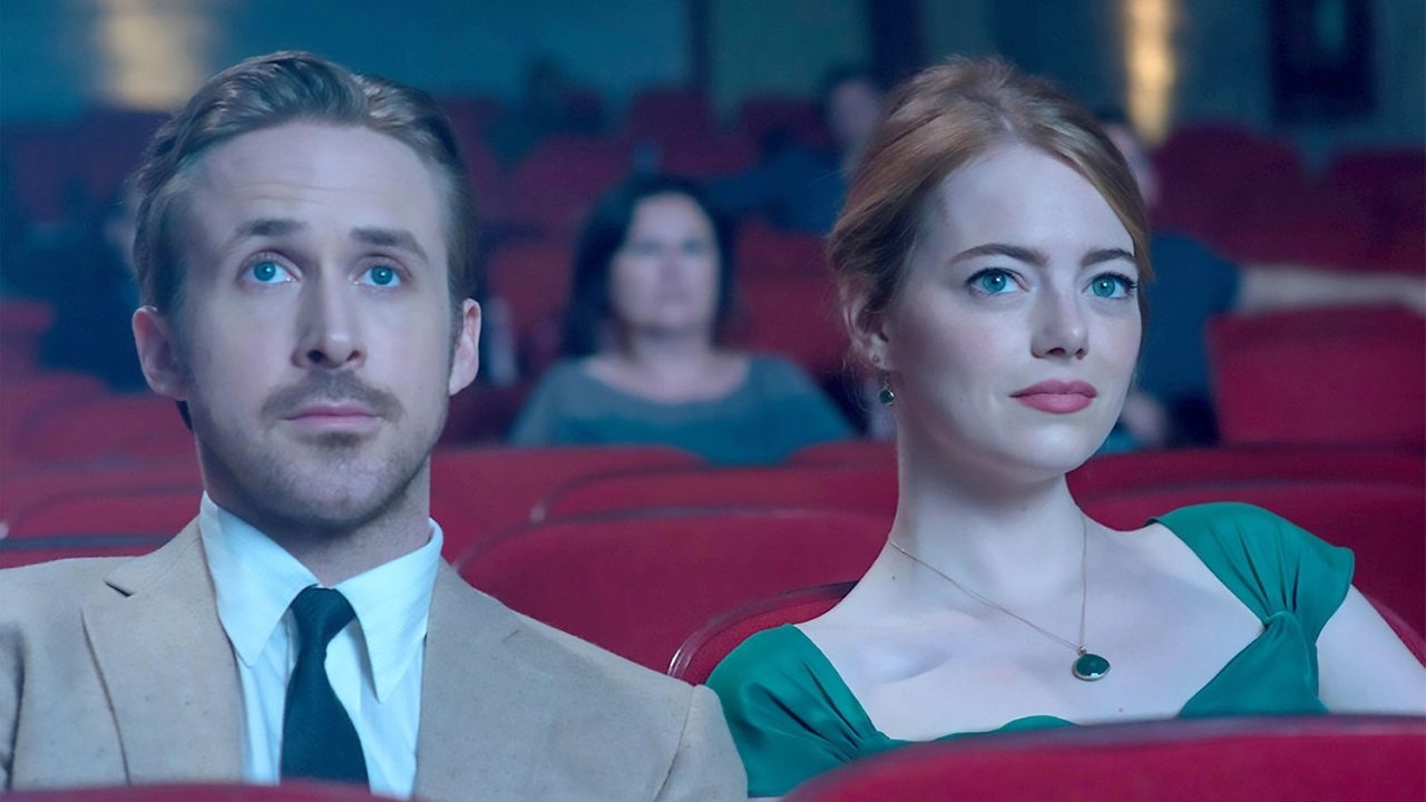 Two actors seated in a theater, the man in a suit and the woman in a green dress