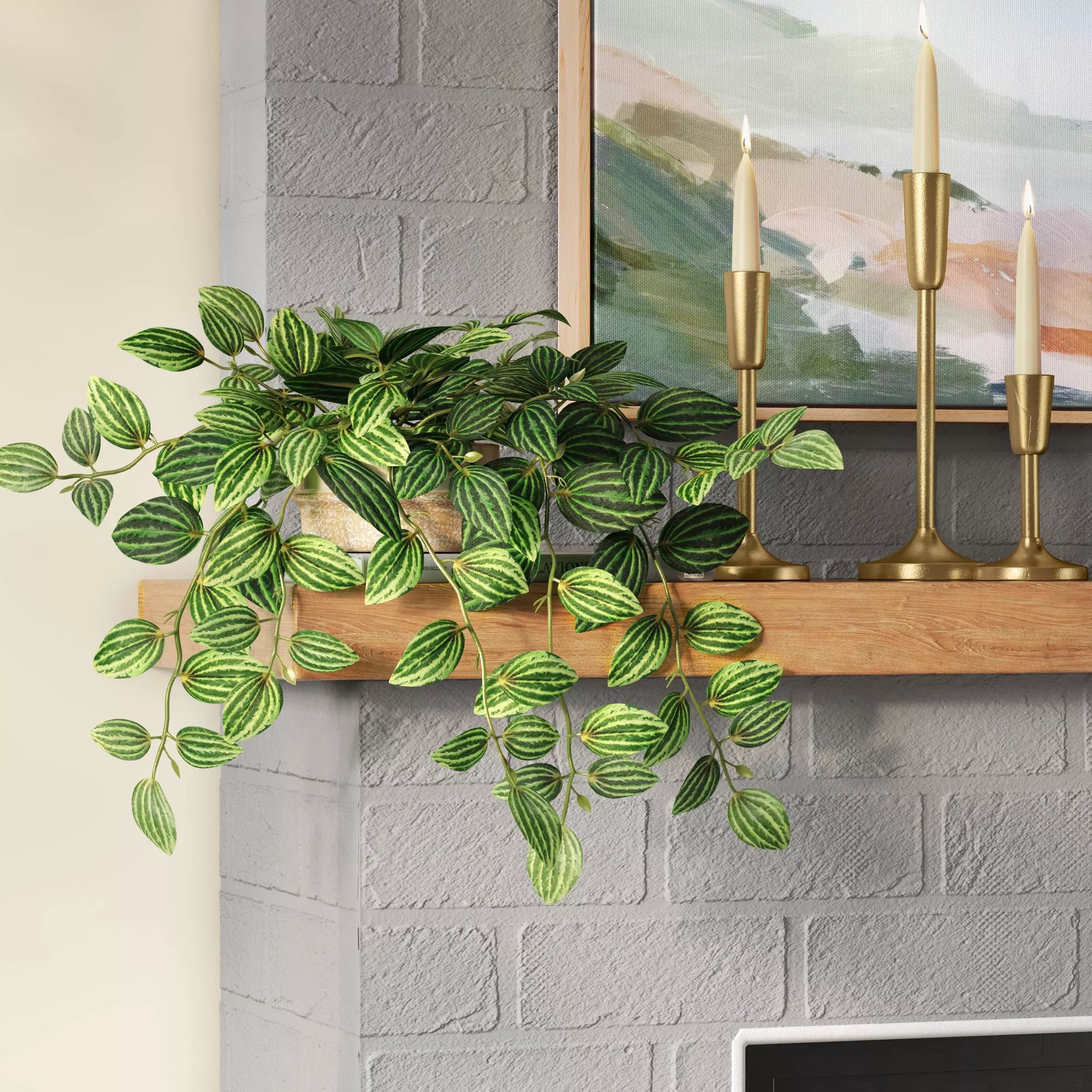 Variegated faux trailing houseplant on a wooden shelf accompanied by a brass candlestick holder