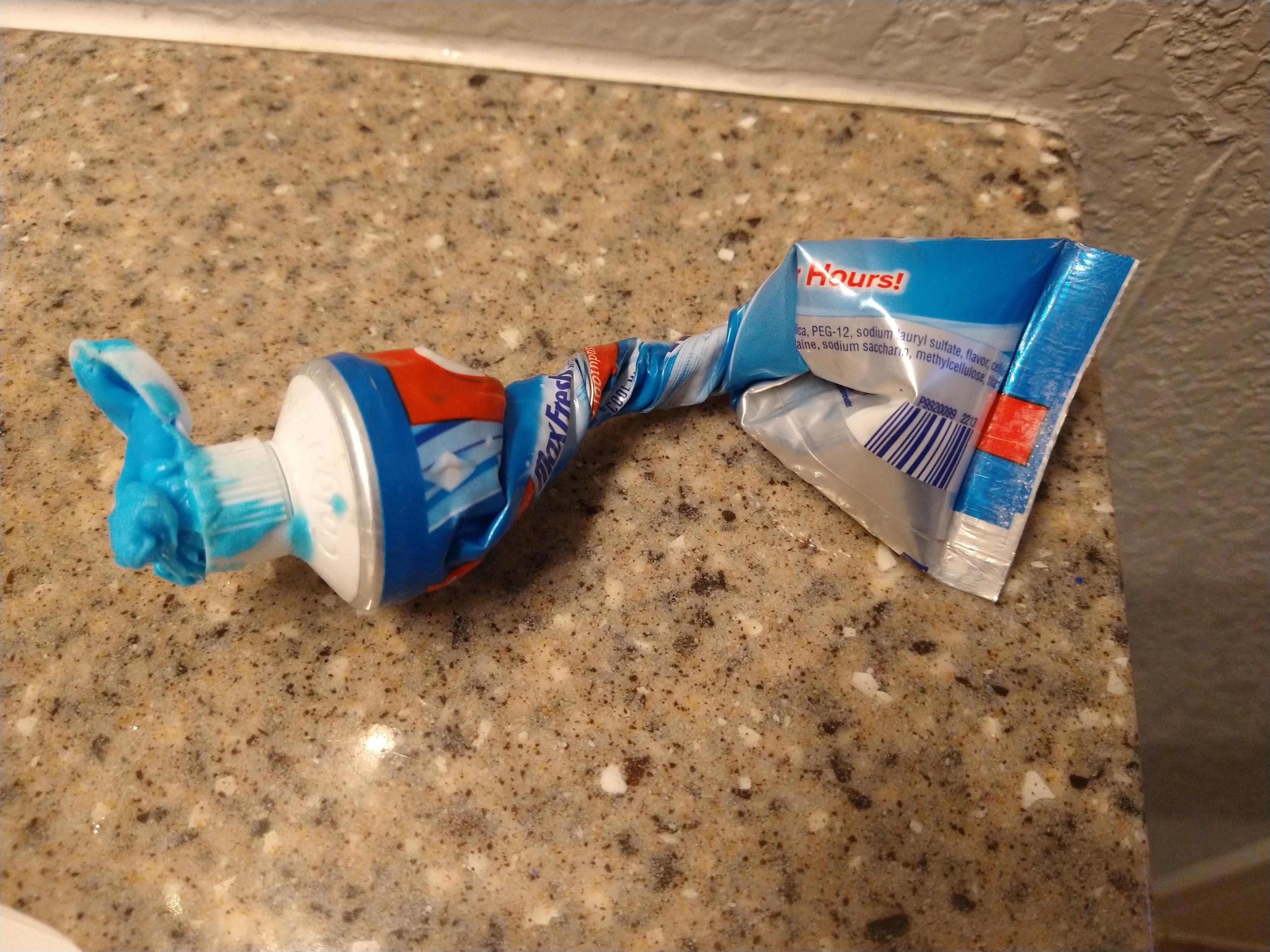 An open toothpaste tube squeezed from the top, with paste overflowing onto a counter