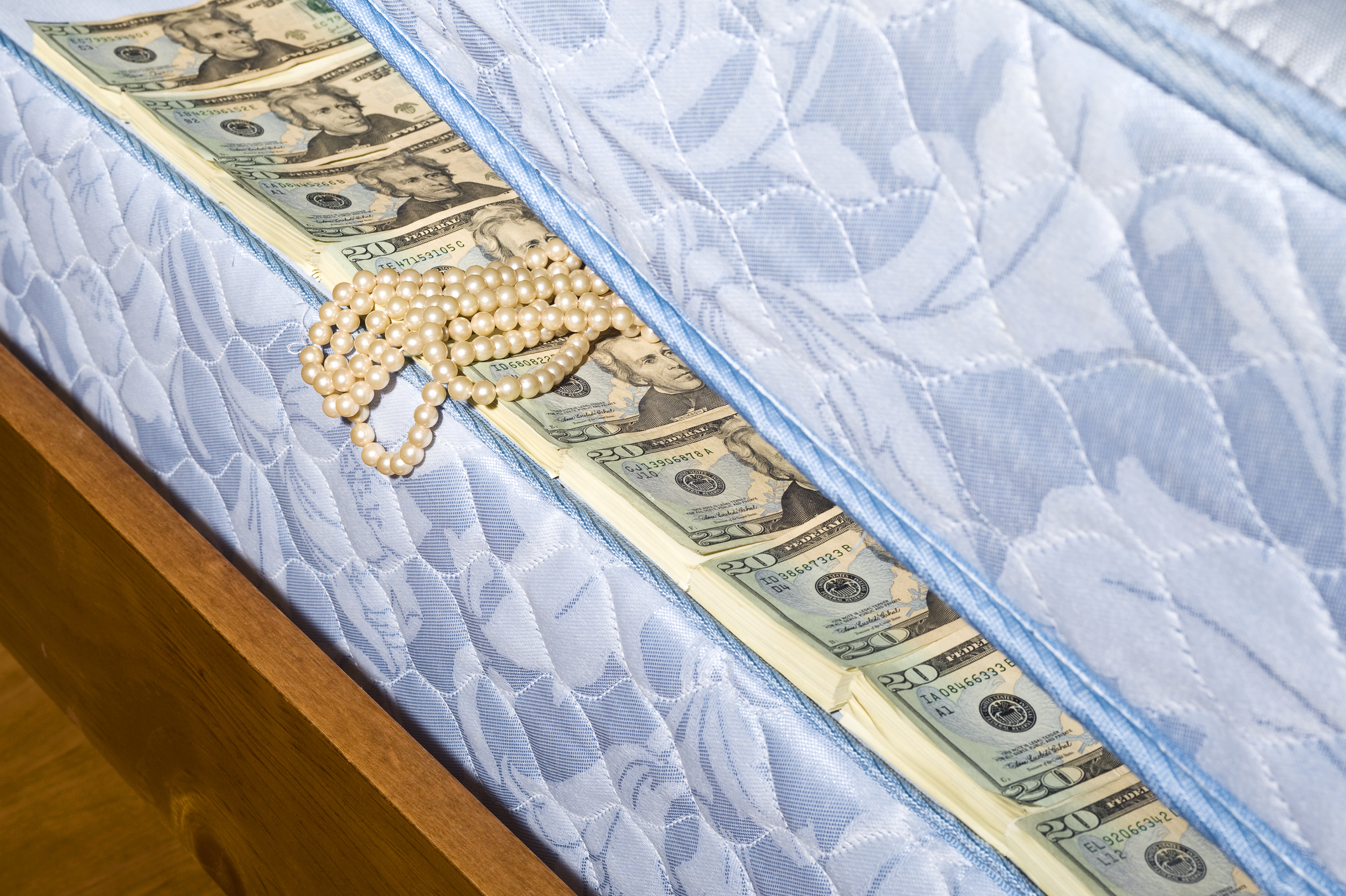 Pearl necklace on a mattress with money stuffed inside, implying hidden savings