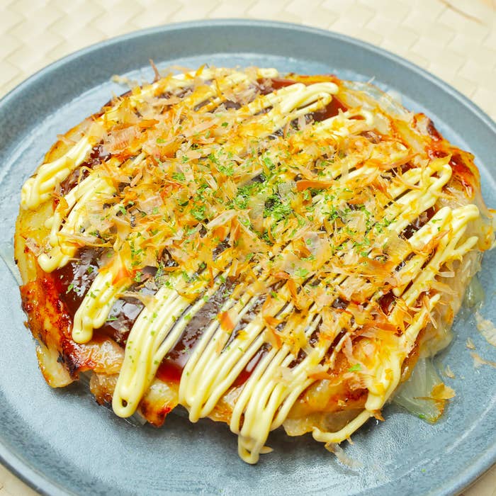 お好み焼きが皿に盛られていて、マヨネーズと青のりがトッピングされています。