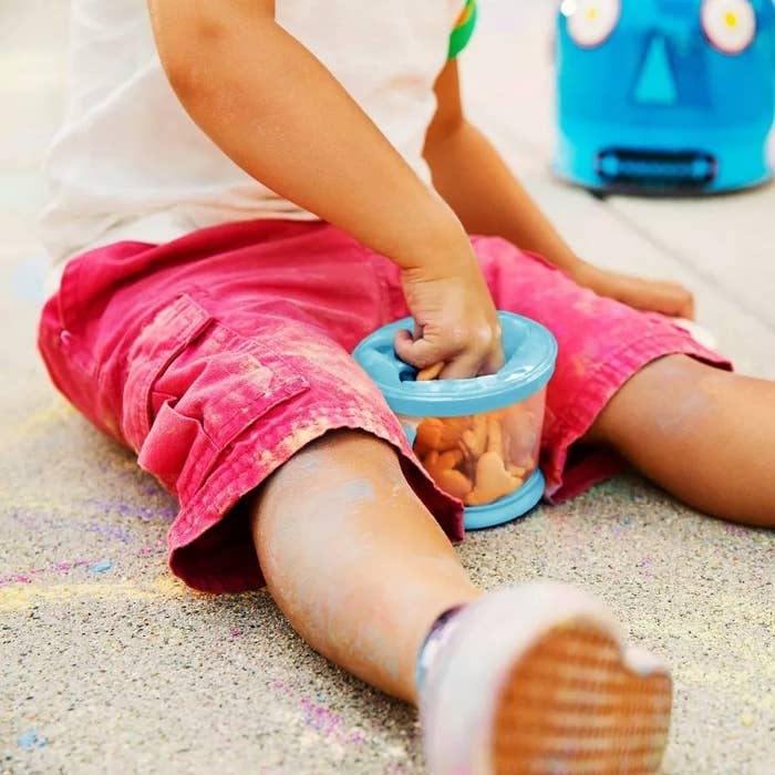 Child playing with a toy on the ground, reaching into a container, with a toy robot nearby